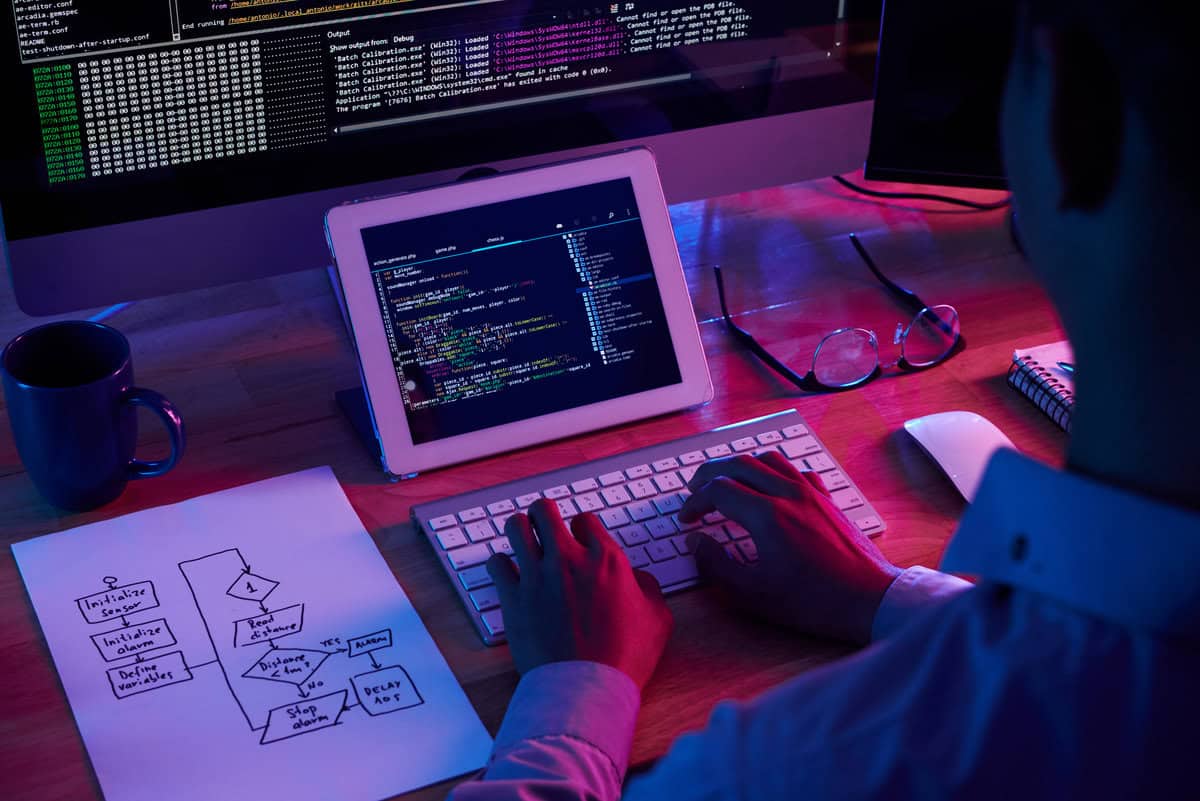 Programista kodujący na tablecie i komputerze stacjonarnym z diagramem przepływu i środowiskiem programistycznym. testimonial