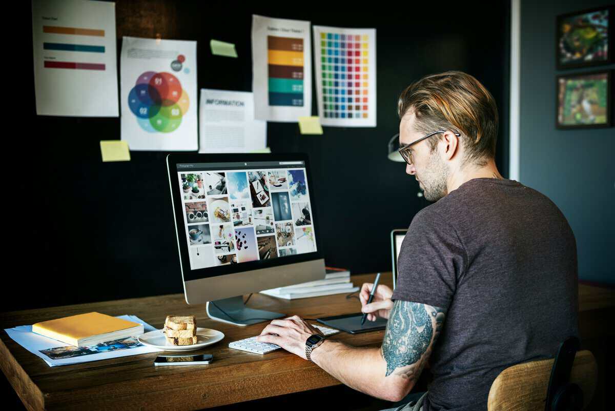 Graphic designer with tattoos working at a desk with a digital tablet and computer. testimonial