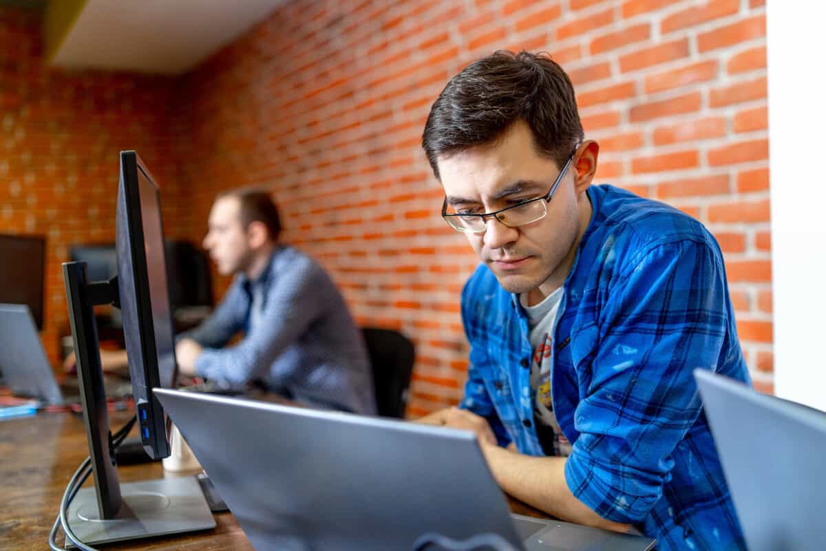 Two male developers sitting side-by-side, working on laptops in a modern office. testimonial