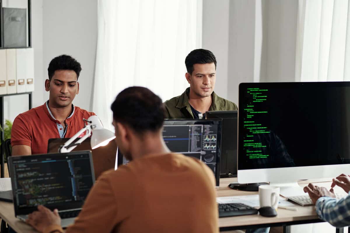 Two male developers sitting side-by-side, working on laptops in a modern office. testimonial