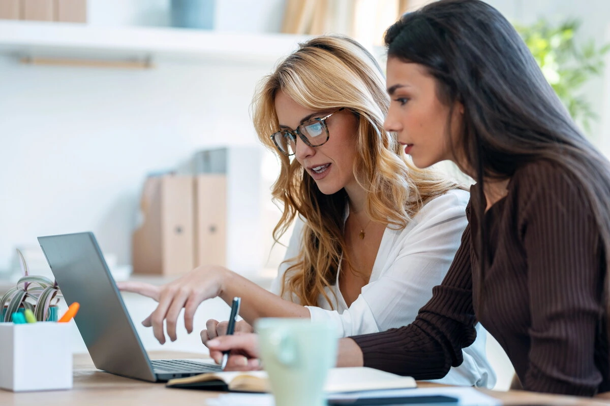 Two female professionals collaborating over a laptop in a modern office.