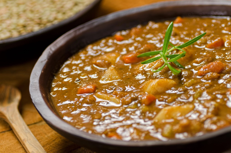 A bowl of Romanian ciorbă, a hearty sour soup with meat, vegetables, and herbs, served in a rustic dish.