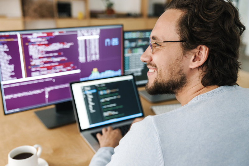 A cheerful caucasian Odoo developer man wearing eyeglasses working with computers in an office.
