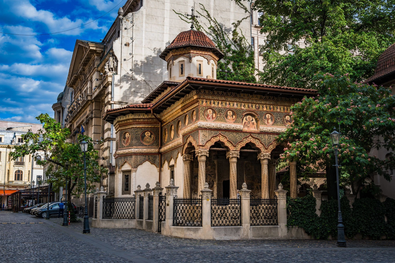 The Stavropoleos Monastery Church in Bucharest, Romania, with its ornate frescoes, arches, and stone columns along a cobblestone street.